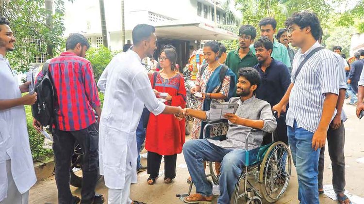 হাসপাতাল থেকে ক্যাম্পাসে এসে হুইলচেয়ারে বসেই ভোটের প্রচারণা চালাচ্ছেন জিএস প্রার্থী মেঘমল্লার বসু। গতকাল মধুর ক্যানটিনের সামনে। ছবি: আজকের পত্রিকা